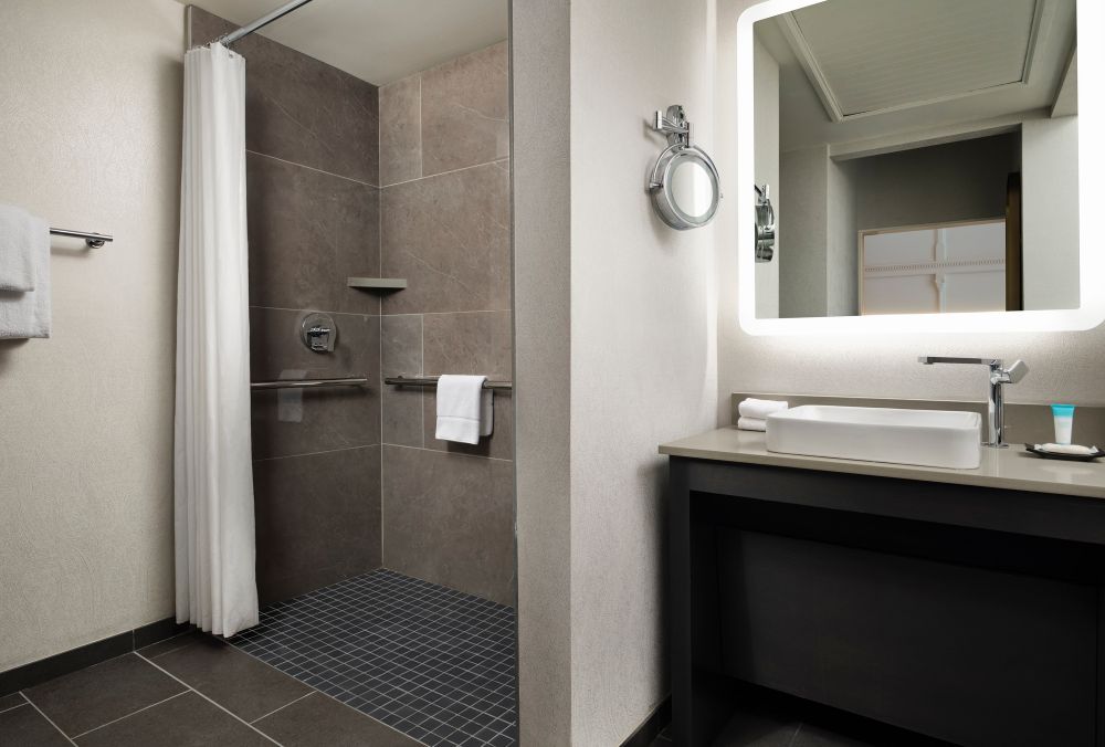 Modern hotel bathroom with a large walk-in shower, featuring a rainfall showerhead, and a handheld shower