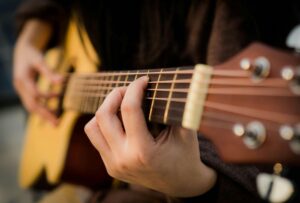 Close-up of a person’s hand playing an acoustic guitar, focusing on the fingers pressing down on the strings and fretboard.