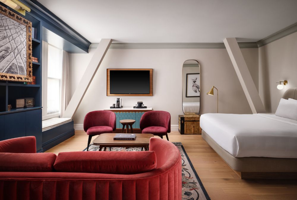 Luxurious hotel room featuring a cozy seating area with vibrant red chairs, a flat-screen TV, and a comfortable king-size bed.