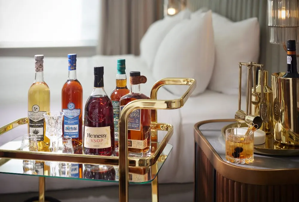 A luxurious hotel room with a minibar trolley showcasing various premium spirits, including Hennessy VSOP
