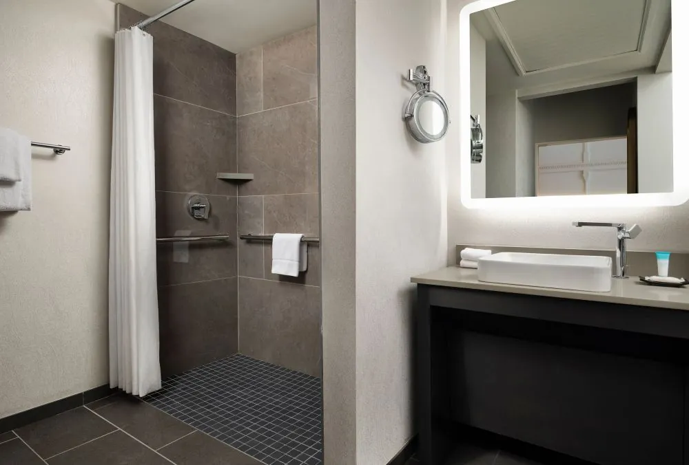 Modern hotel bathroom with a large walk-in shower, featuring a rainfall showerhead, and a handheld shower