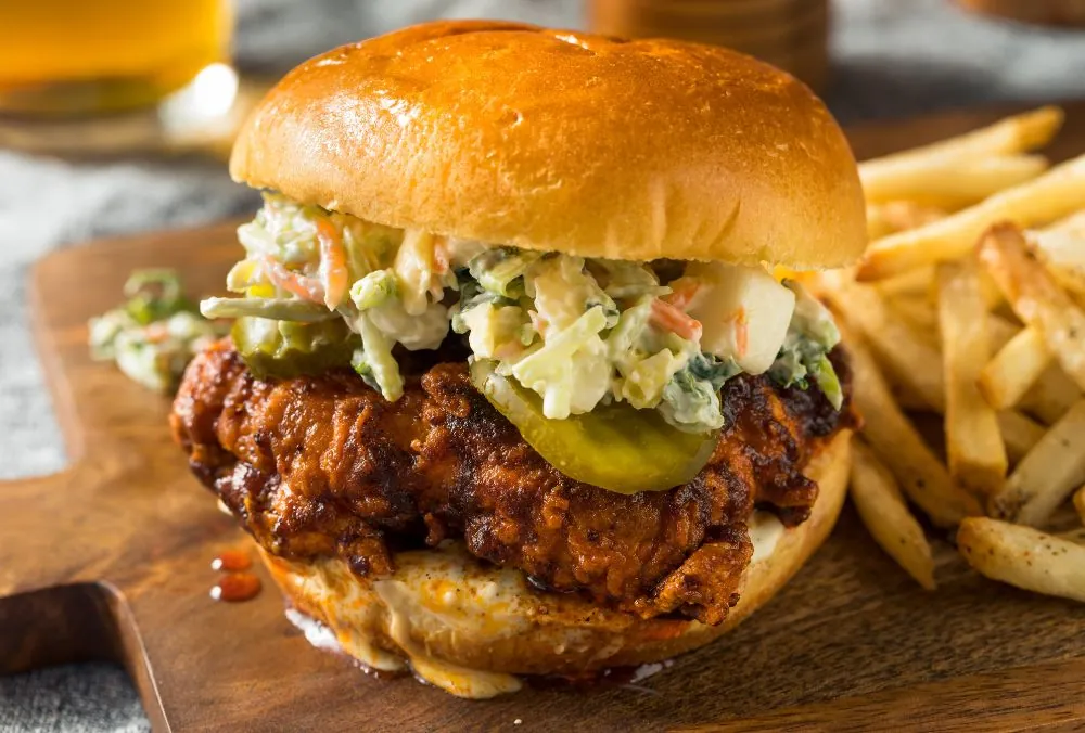 A close-up of a crispy fried chicken sandwich topped with pickles and creamy coleslaw
