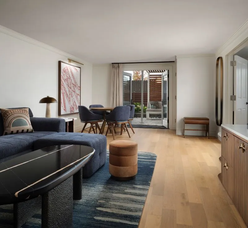 A luxurious living area in a hotel suite, featuring a blue sectional sofa, a dining table and a private terrace